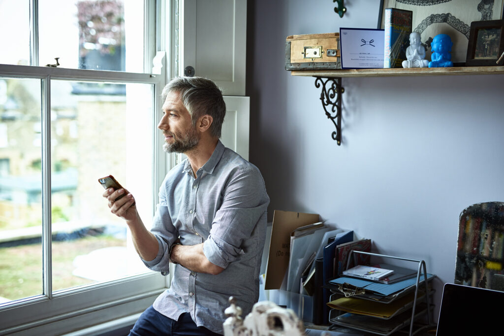 Image of man looking out the window, contemplating, working remotely through online tools