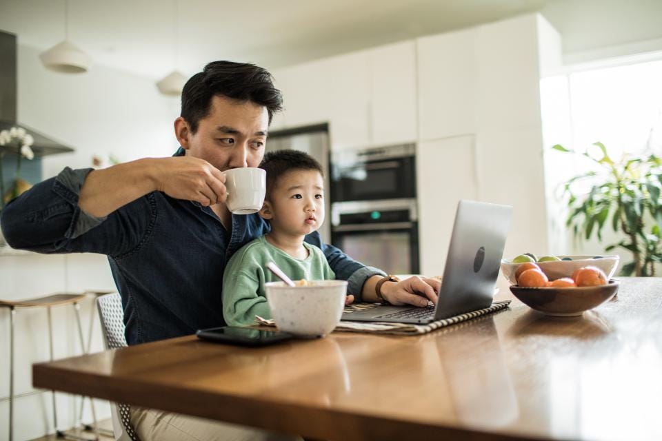 Photo of dad working from home at dining table with son on lap for home workspace